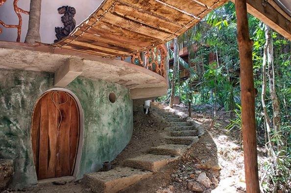 Hobbit-style arched wooden door and stone steps below the earth bag home at Better in Belize