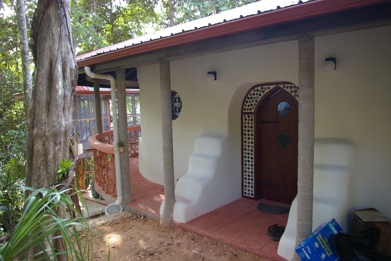 Arched wooden front door framed with glass bottles on the porch of the earth bag home at Better in Belize