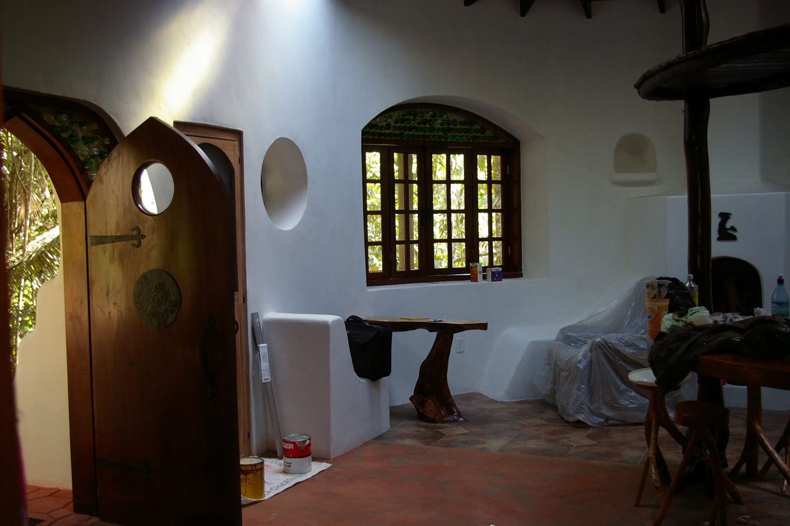 Inside the earth bag home: curved white walls, round window, bottle-glass arch and handmade wood furniture
