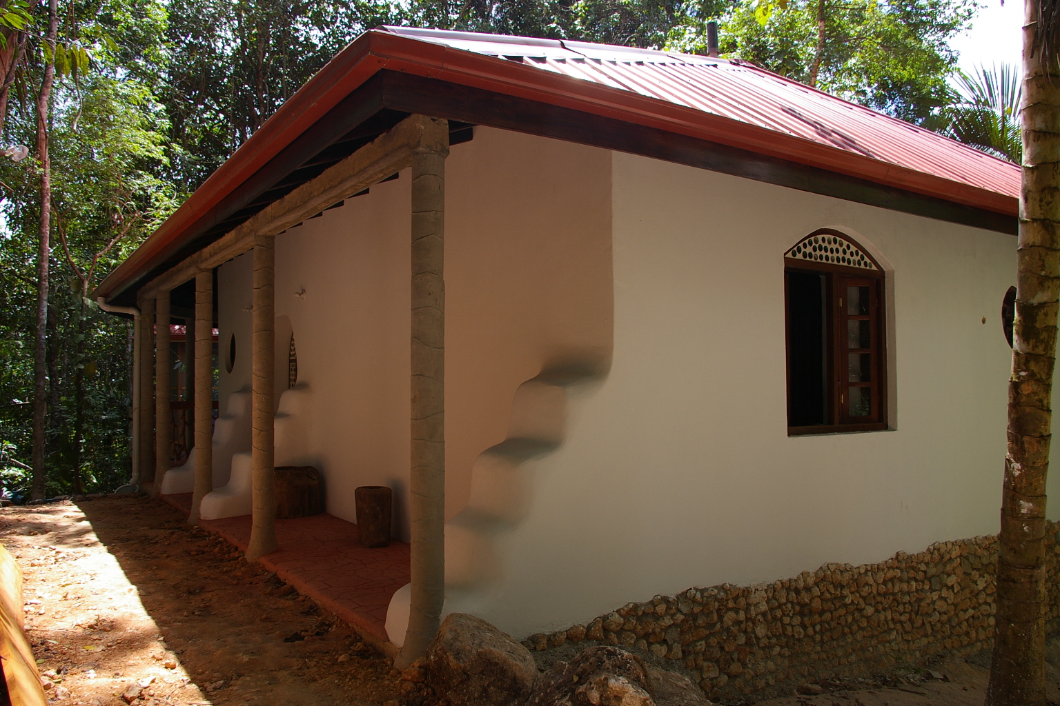White earth bag home with a red metal roof and covered porch in the jungle at Better in Belize