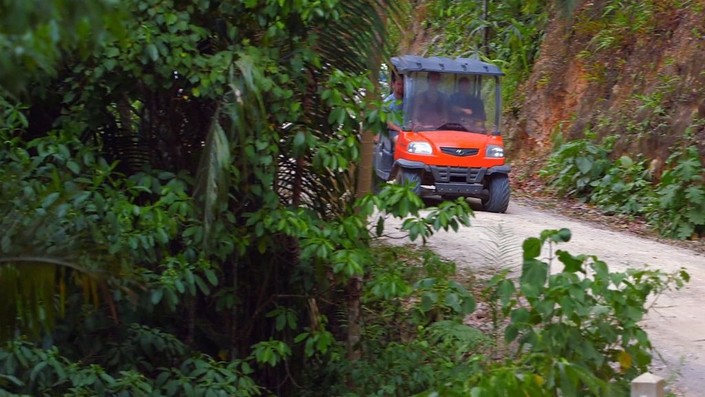 Orange Kubota utility cart driving along a forested hillside road at Better in Belize