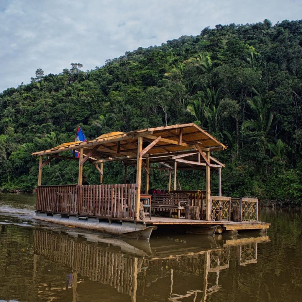 Pontoon boat on the river surrounded by jungle-covered hills, Better in Belize