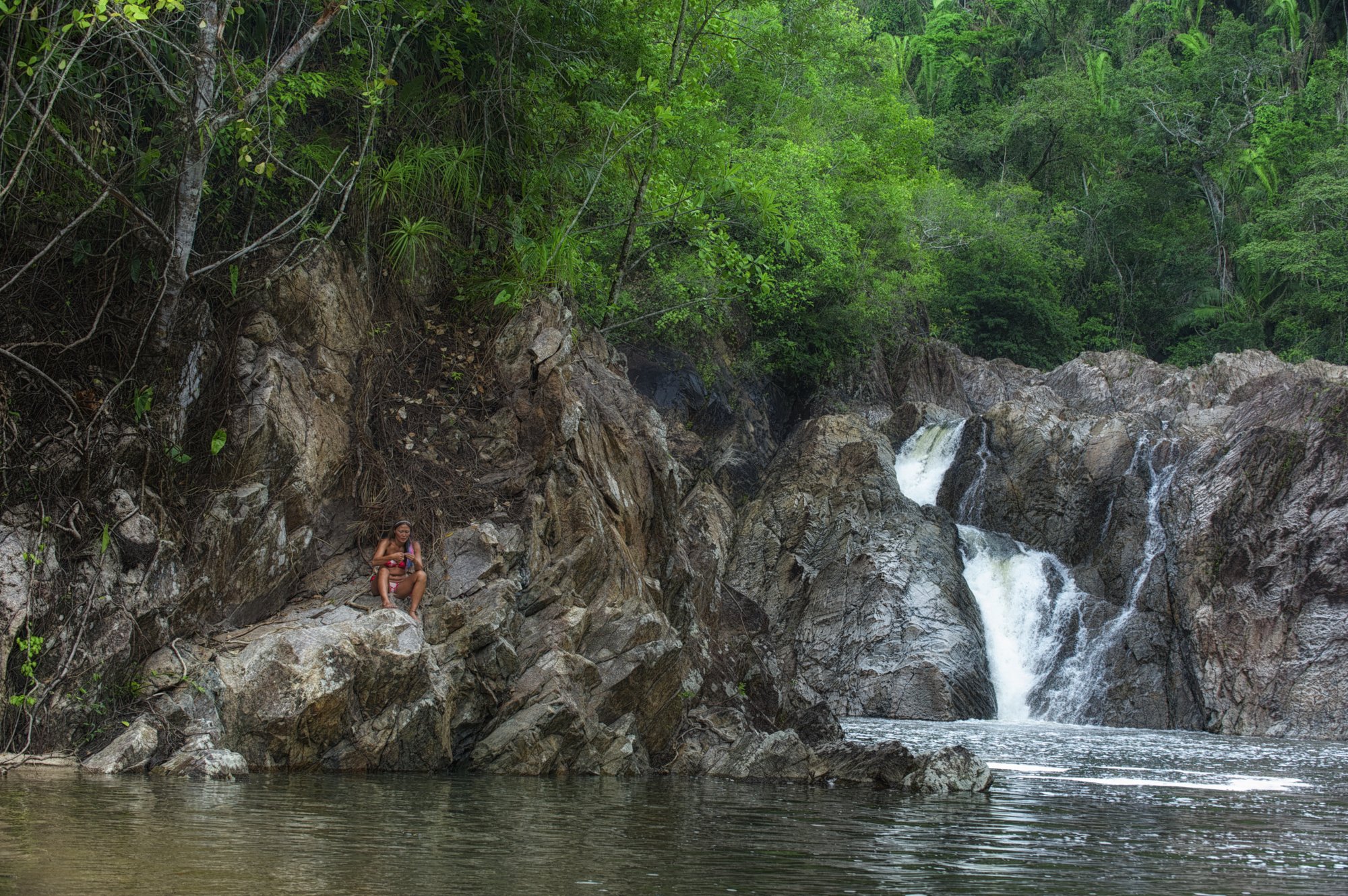 Woman sitting on the rocks beside a waterfall and river pool